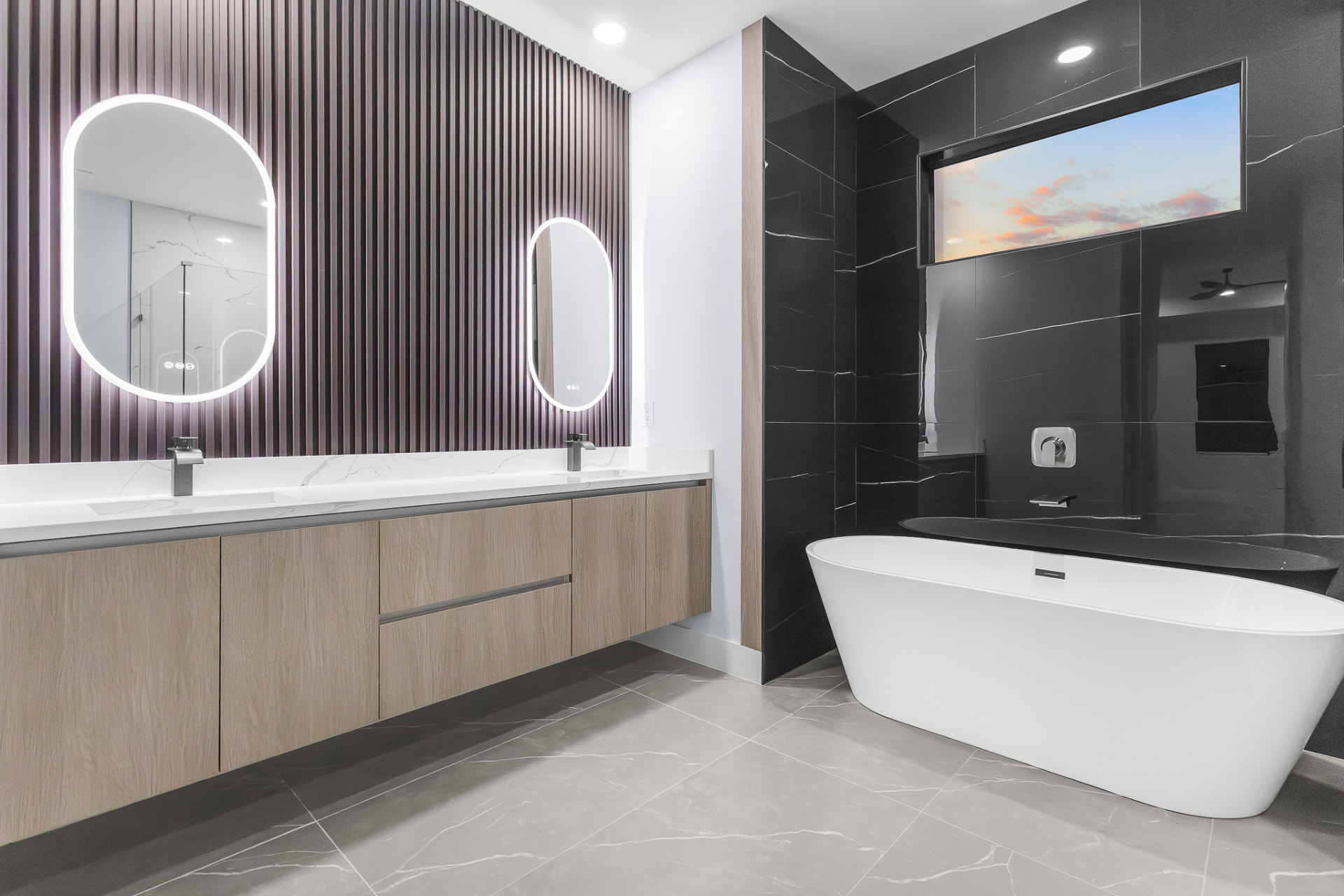 Primary bathroom with floating wood vanity, backlit mirrors and freestanding tub