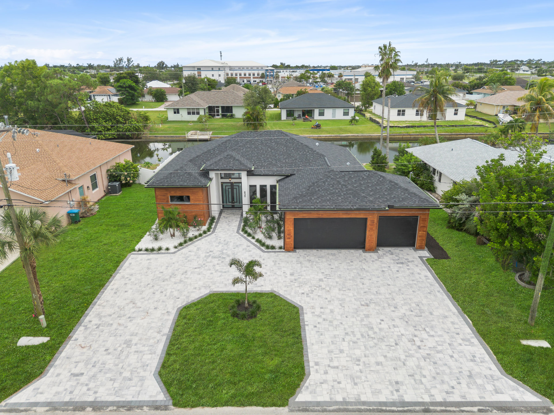 Elevated drone view of a modern home with paver driveway and lake behind