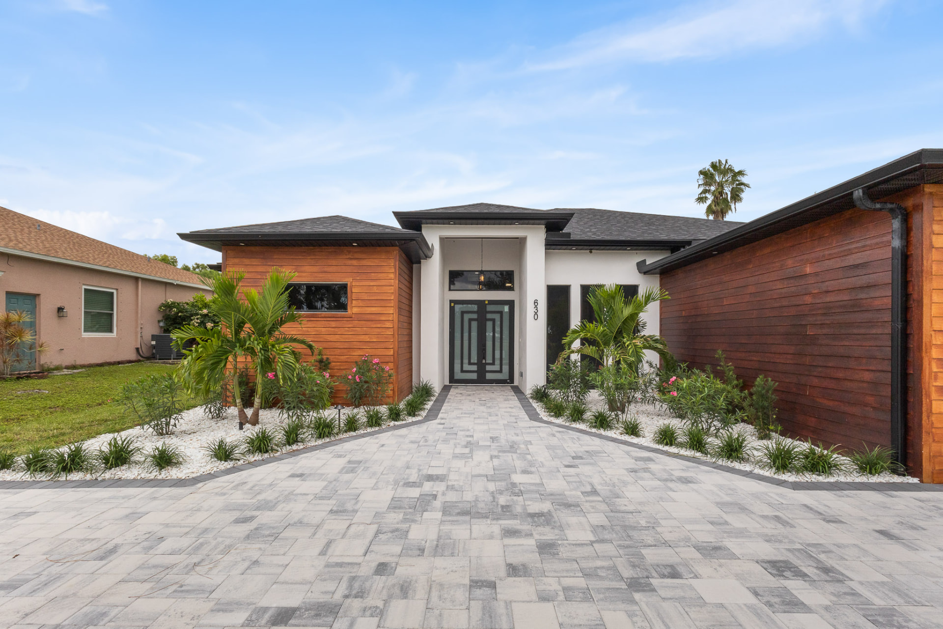 Covered entry with black glass double doors and tropical landscaping