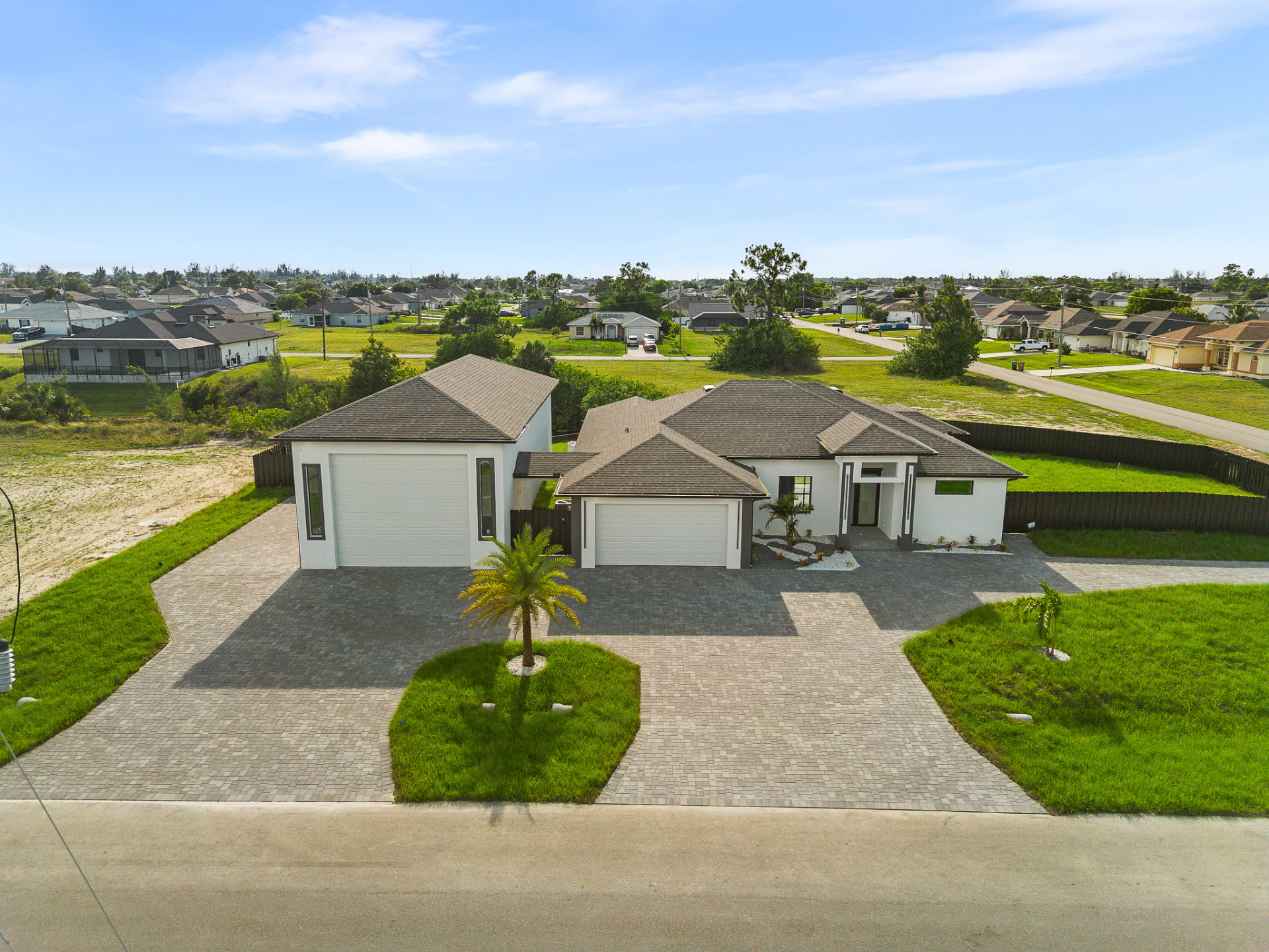 Wide aerial drone view of a home with oversized driveway and open land