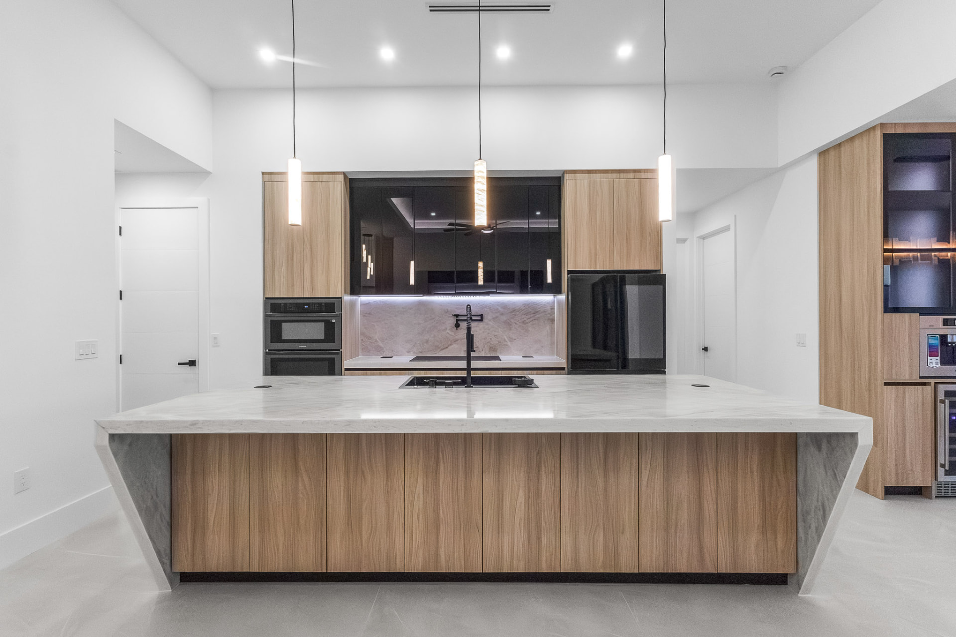 Modern kitchen with waterfall marble island, wood cabinetry and pendant lights