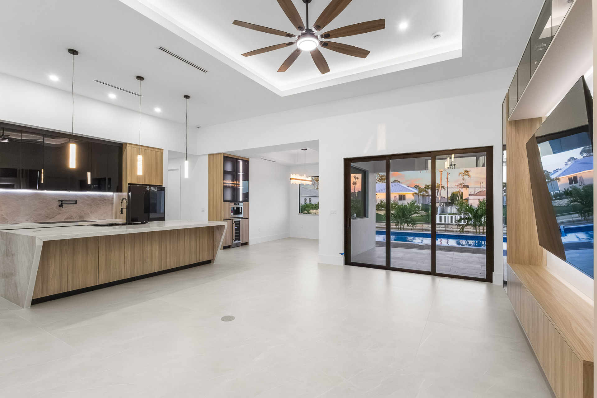 Open-plan living room and kitchen with sliding glass doors to the pool at sunset